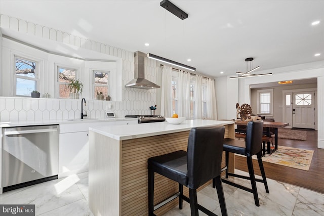 kitchen featuring a sink, light countertops, appliances with stainless steel finishes, wall chimney exhaust hood, and tasteful backsplash