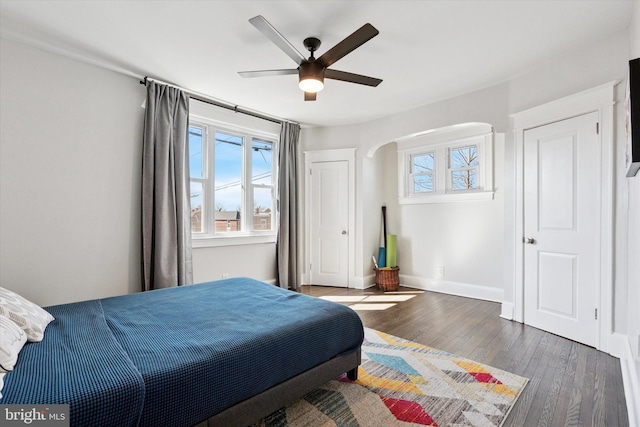 bedroom featuring ceiling fan, baseboards, arched walkways, and hardwood / wood-style floors