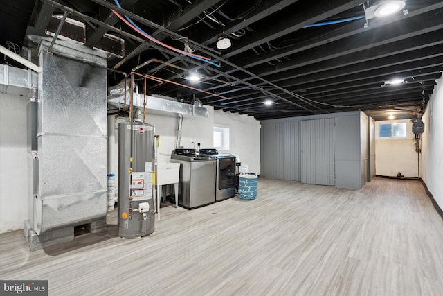 basement with washing machine and clothes dryer, a healthy amount of sunlight, water heater, and wood finished floors