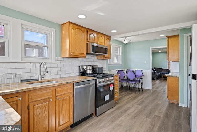 kitchen featuring light stone countertops, a sink, stainless steel appliances, light wood-style floors, and tasteful backsplash