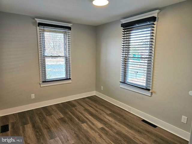 spare room featuring dark wood finished floors, visible vents, and baseboards