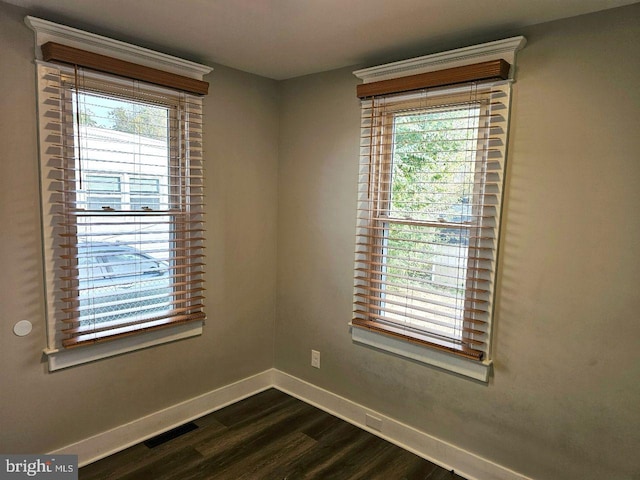 spare room featuring visible vents, baseboards, and dark wood-style flooring