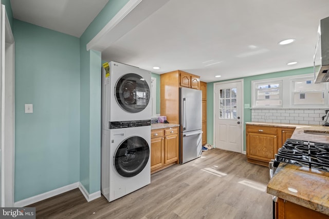 clothes washing area featuring baseboards, laundry area, stacked washing maching and dryer, light wood-style floors, and a sink