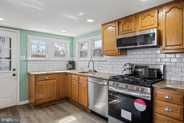 kitchen featuring brown cabinets, light wood-style flooring, a sink, appliances with stainless steel finishes, and light stone countertops