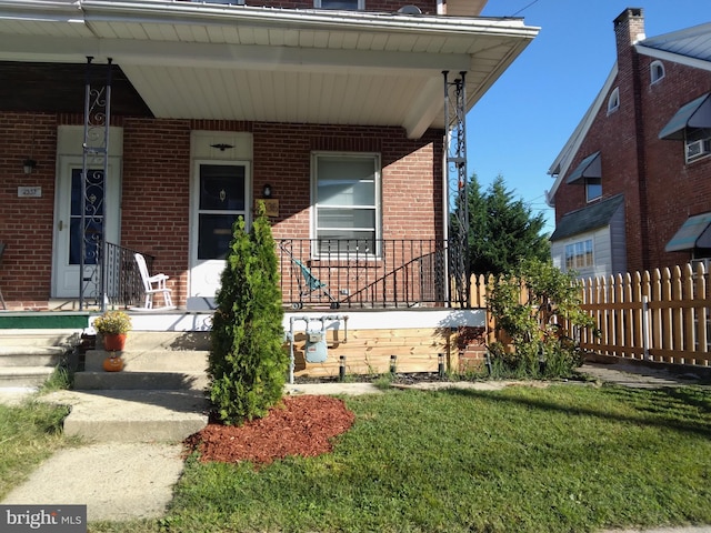 view of front of home with brick siding, a porch, a front yard, and fence