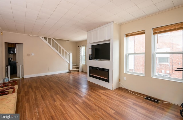 unfurnished living room featuring a glass covered fireplace, stairway, visible vents, and a wealth of natural light