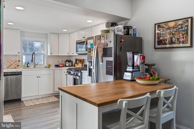 kitchen featuring light wood-style flooring, a sink, tasteful backsplash, white cabinetry, and appliances with stainless steel finishes