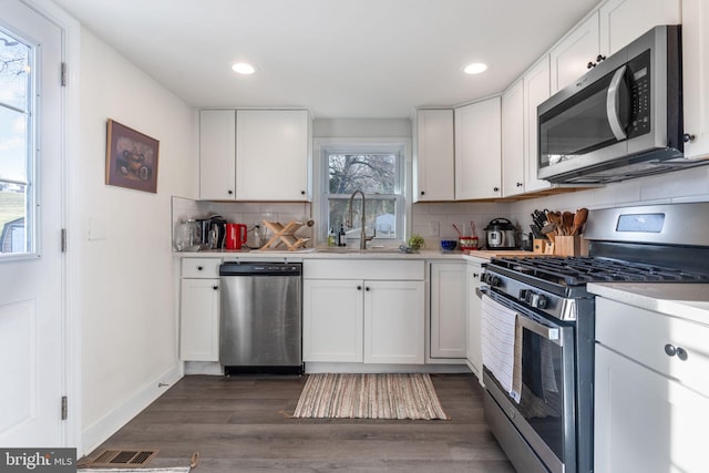 kitchen with a sink, decorative backsplash, light countertops, dark wood-type flooring, and stainless steel appliances