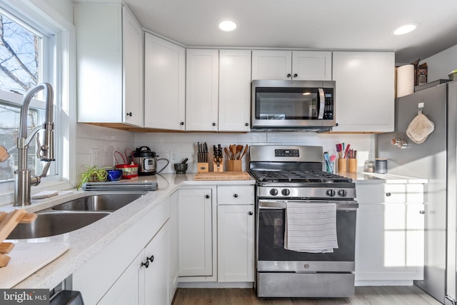 kitchen with backsplash, light stone countertops, appliances with stainless steel finishes, white cabinets, and a sink