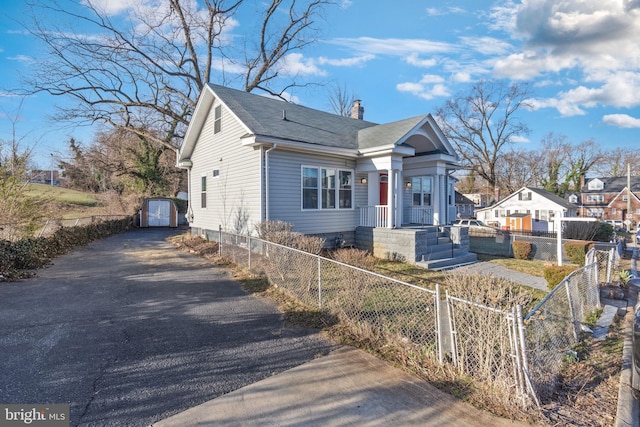 view of front of home with an outbuilding, roof with shingles, driveway, a chimney, and a fenced front yard