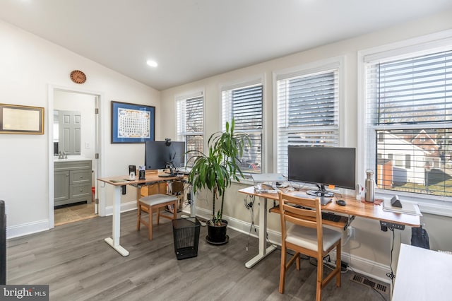 office area featuring wood finished floors, visible vents, baseboards, lofted ceiling, and a sink