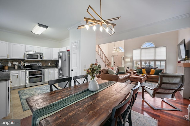 dining space with stairs, light wood-style flooring, a chandelier, and crown molding