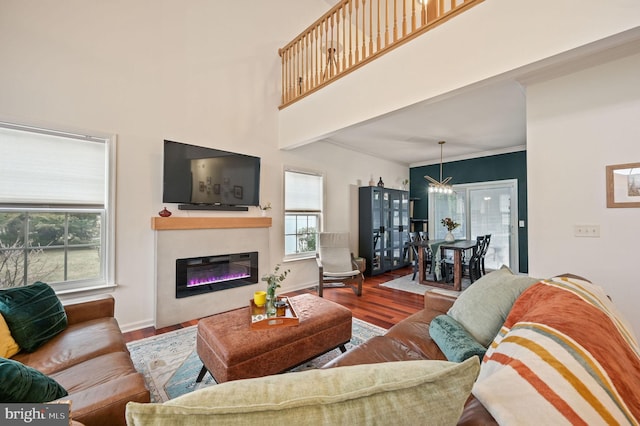 living room featuring crown molding, baseboards, a towering ceiling, wood finished floors, and a glass covered fireplace