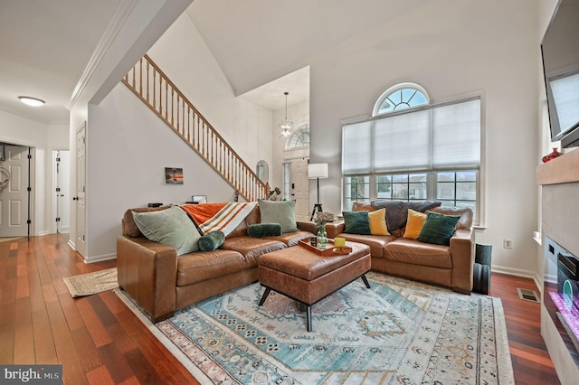 living room featuring hardwood / wood-style floors, baseboards, ornamental molding, stairs, and a towering ceiling