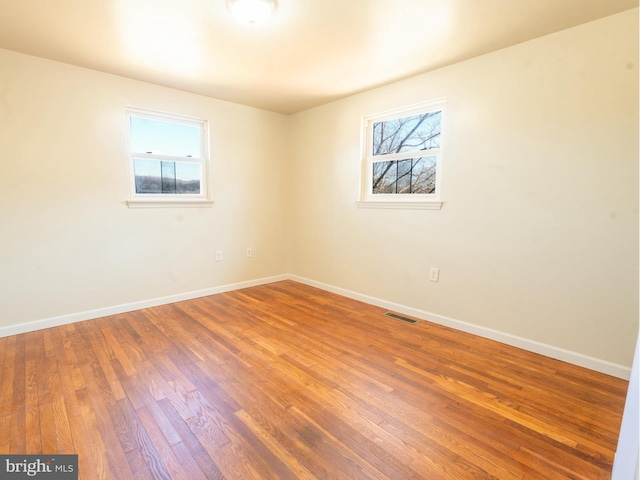 empty room featuring plenty of natural light, wood finished floors, visible vents, and baseboards