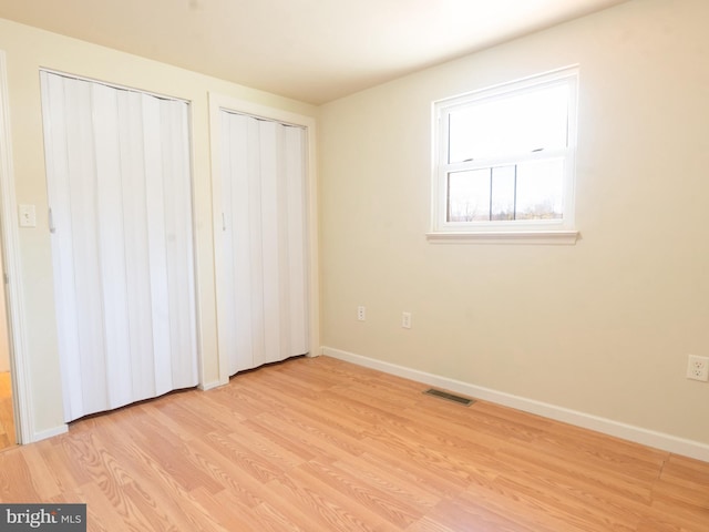 unfurnished bedroom featuring baseboards, visible vents, light wood finished floors, and multiple closets