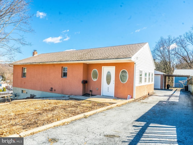 exterior space with a shingled roof, a chimney, a garage, an outdoor structure, and driveway