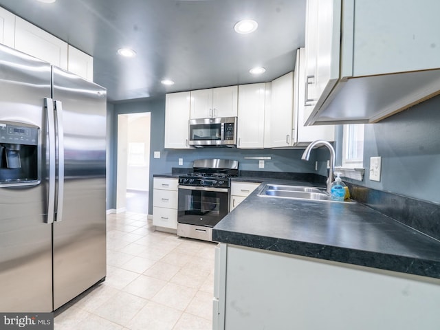 kitchen featuring light tile patterned floors, a sink, stainless steel appliances, white cabinetry, and dark countertops