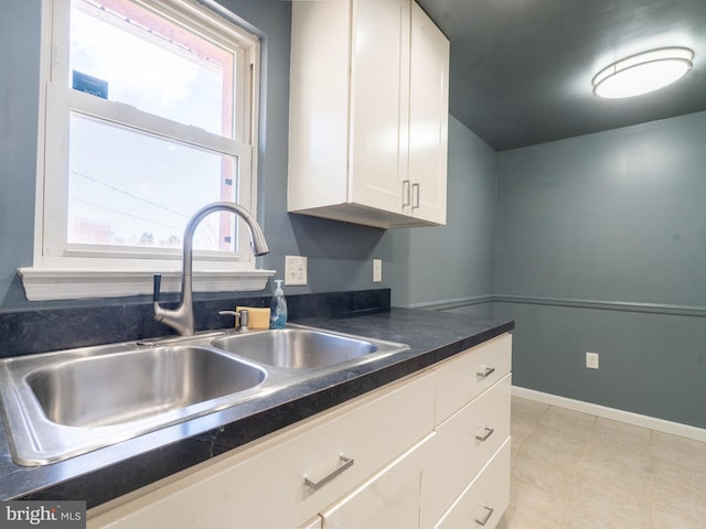 kitchen featuring dark countertops, white cabinets, baseboards, and a sink