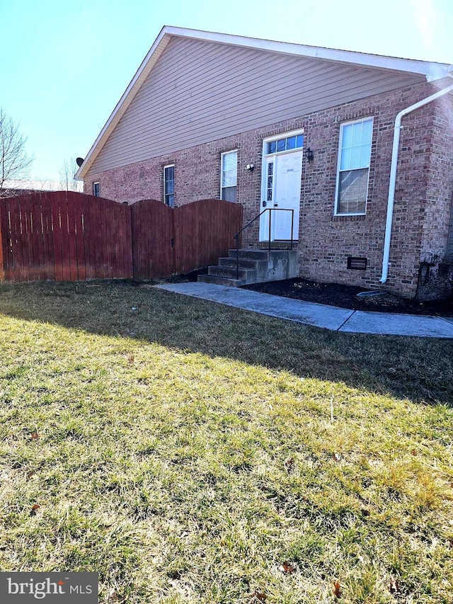 view of front of home featuring a front lawn, fence, brick siding, and crawl space