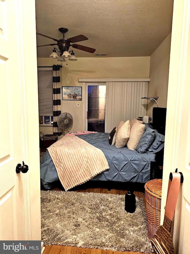 bedroom with visible vents, a textured ceiling, wood finished floors, and a ceiling fan