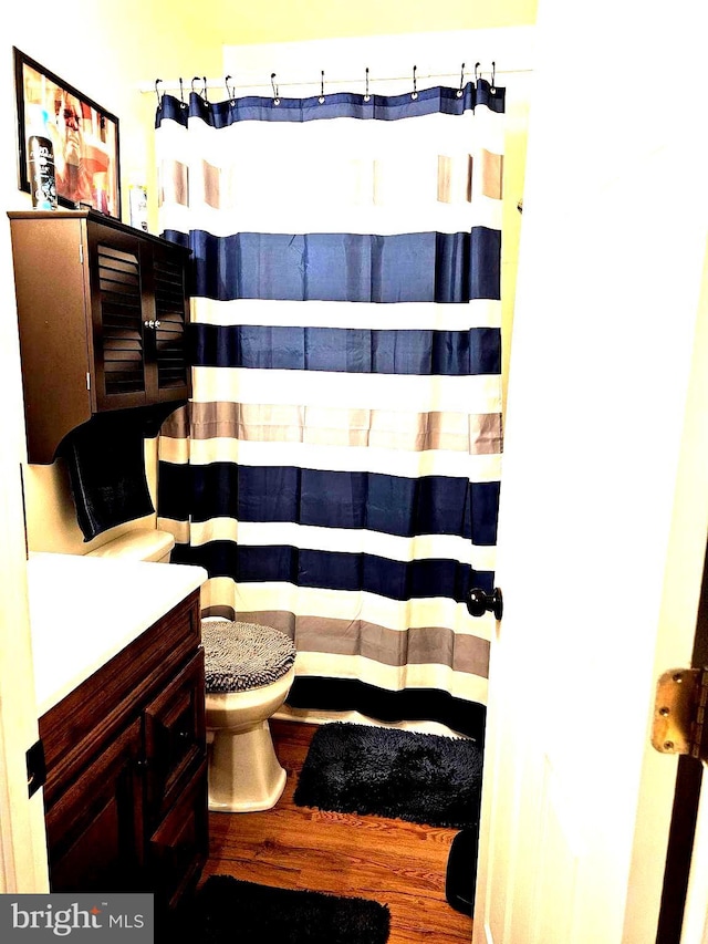 bathroom featuring curtained shower, toilet, vanity, and wood finished floors