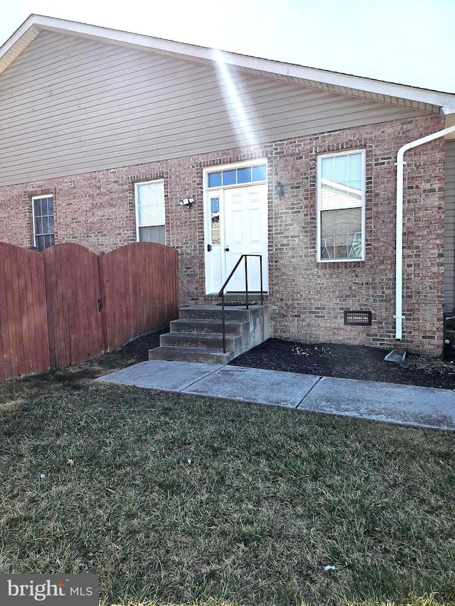 view of front of home with crawl space, brick siding, a front yard, and fence