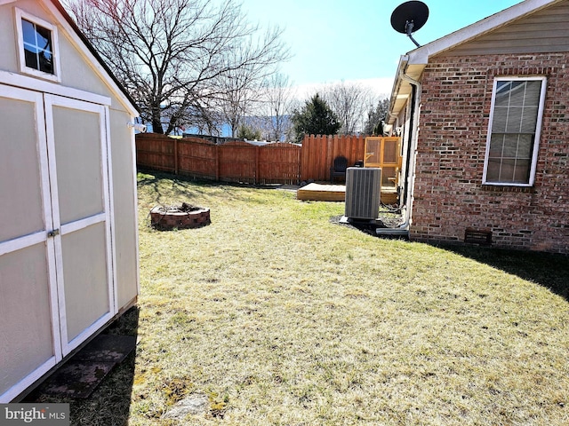 view of yard featuring central air condition unit, an outbuilding, an outdoor fire pit, fence, and a storage shed