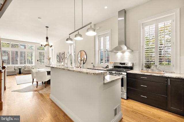 kitchen with wall chimney exhaust hood, stainless steel range with gas cooktop, light wood-style flooring, and a healthy amount of sunlight