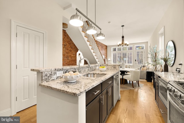 kitchen featuring a sink, an island with sink, light wood-style floors, an inviting chandelier, and appliances with stainless steel finishes