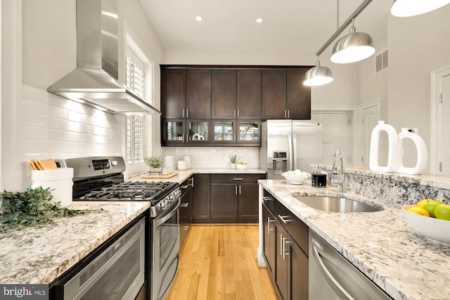 kitchen featuring dark brown cabinets, visible vents, a sink, wall chimney exhaust hood, and appliances with stainless steel finishes