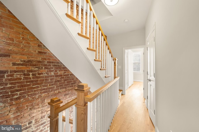 hall featuring light wood finished floors, brick wall, and stairway