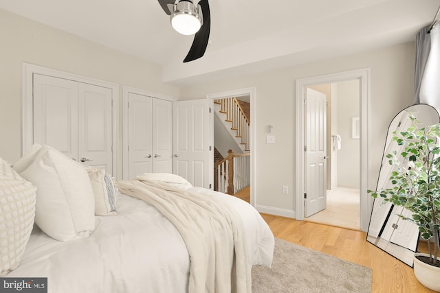 bedroom with a ceiling fan, connected bathroom, two closets, light wood-style flooring, and baseboards