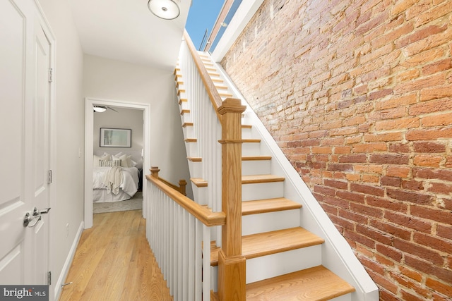 stairway with brick wall, baseboards, and wood finished floors