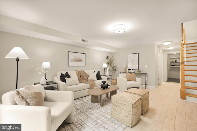 living room with baseboards, visible vents, light wood finished floors, and stairs