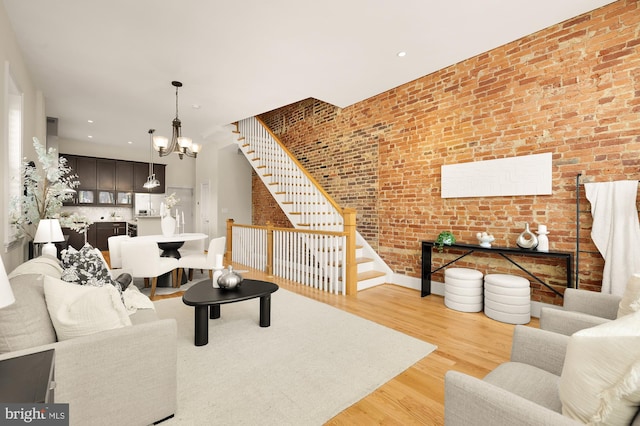 living room featuring recessed lighting, wood finished floors, a chandelier, stairs, and brick wall