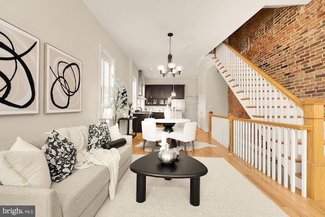 living room with stairs, brick wall, a chandelier, and light wood-style floors