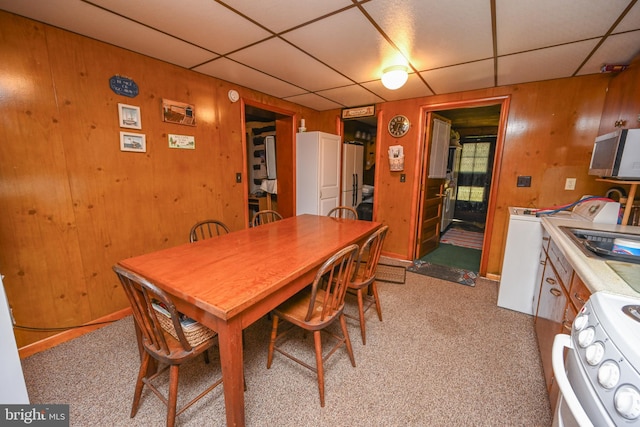 dining area featuring a drop ceiling, wooden walls, and light colored carpet