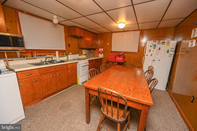 kitchen with a sink, a drop ceiling, white appliances, and wood walls