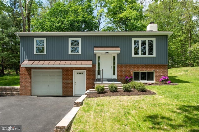 split foyer home featuring driveway, a standing seam roof, a front yard, an attached garage, and a chimney