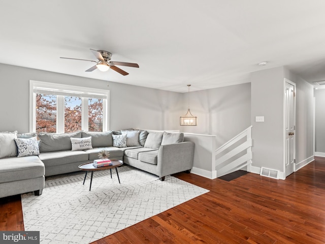 living area featuring ceiling fan with notable chandelier, dark wood-style floors, visible vents, and baseboards