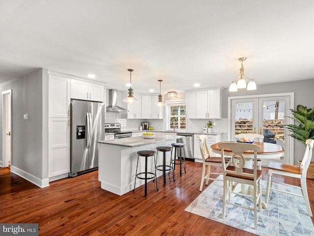 kitchen with tasteful backsplash, a kitchen island, stainless steel appliances, white cabinets, and wall chimney range hood