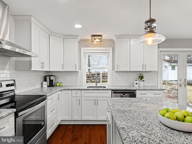 kitchen with appliances with stainless steel finishes, white cabinetry, wall chimney range hood, and a sink