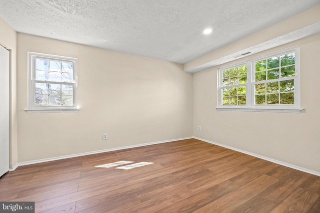 empty room featuring a wealth of natural light, visible vents, baseboards, and wood finished floors