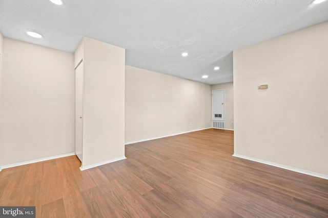 empty room featuring recessed lighting, wood finished floors, baseboards, and a textured ceiling