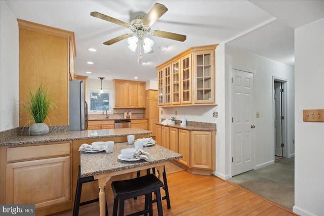 kitchen with light brown cabinets, appliances with stainless steel finishes, light wood-style floors, and a peninsula