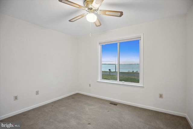 empty room featuring visible vents, baseboards, a water view, carpet flooring, and a ceiling fan