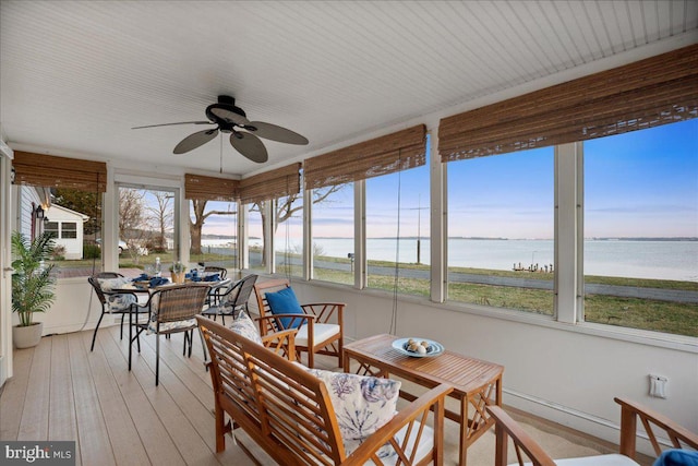 sunroom with a ceiling fan and a water view