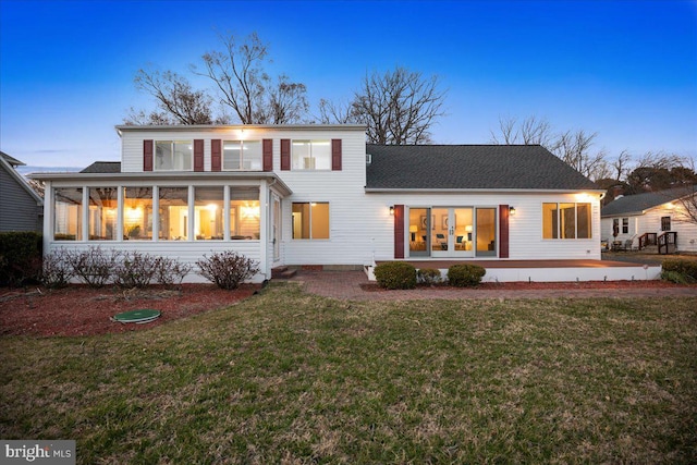 rear view of house with a patio area, a lawn, a sunroom, and roof with shingles