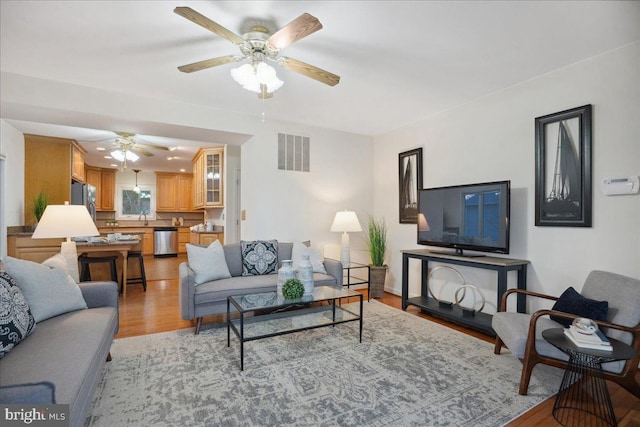 living room featuring a ceiling fan, visible vents, and light wood finished floors